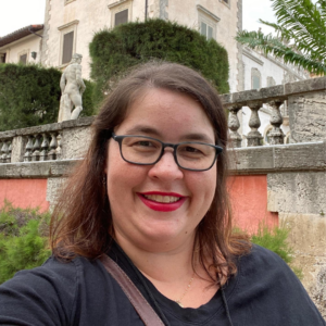 woman smiles standing in front of gardens and old building